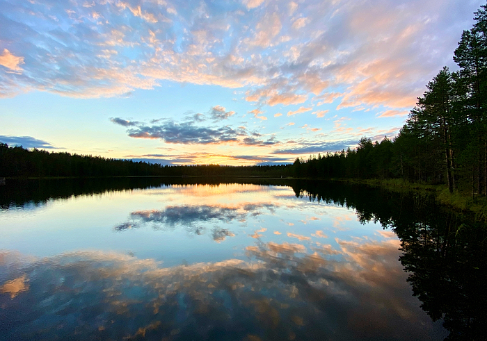 Auringonlaskun ja pilvien heijastuma järven pintaan Hossan kansallispuistossa.
