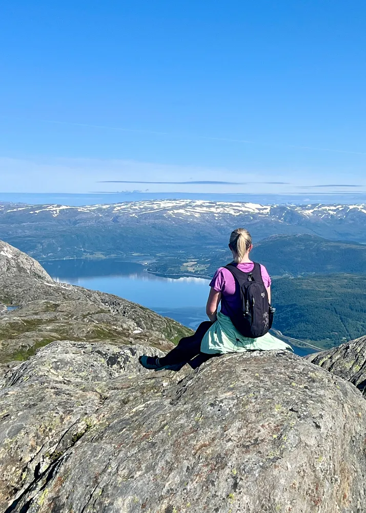 Helglandstrappan Øyfjelletin huipulla istumassa kalliolla. Taustalla meri ja lumihuippuiset vuoret.